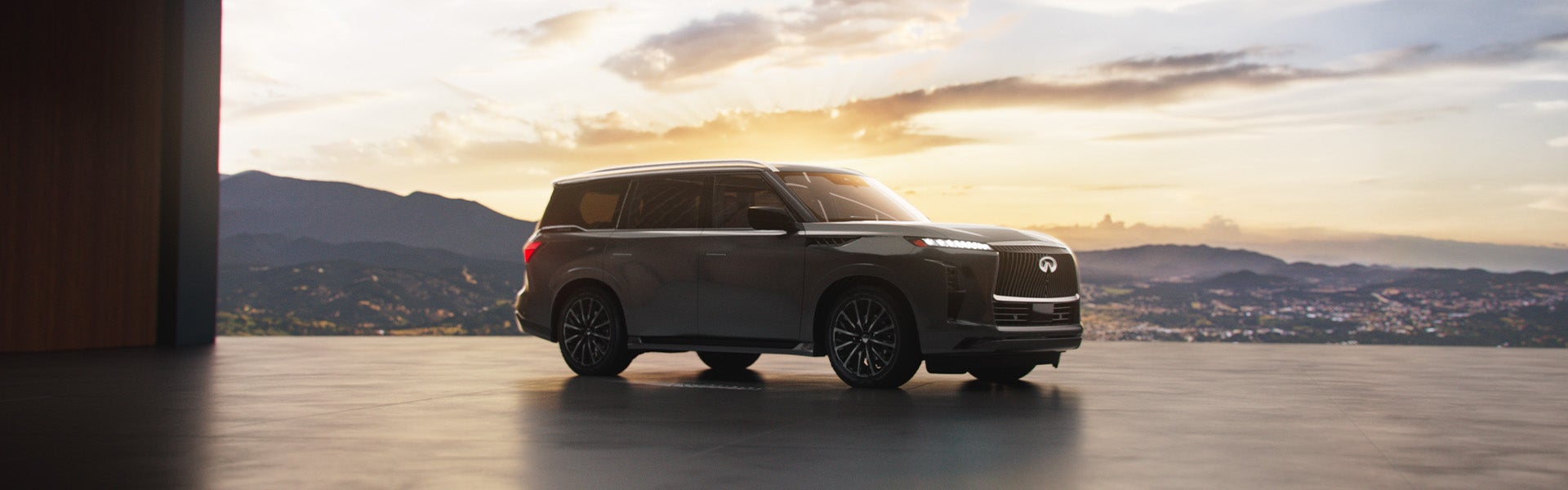 A dark-colored INFINITI QX80 parked indoors with a scenic sunset and mountains visible